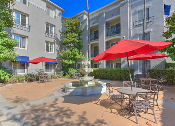 A patio with a table, chairs and umbrellas in front of a building.