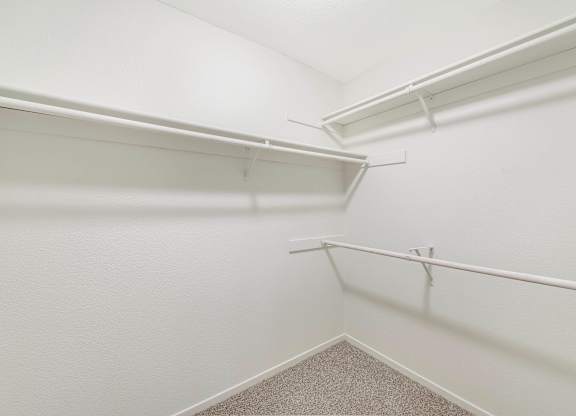 A white closet with a carpeted floor and white shelves.