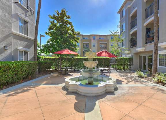 A courtyard with a fountain and red umbrellas.
