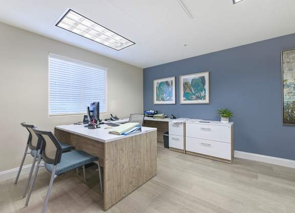A room with a desk, chair, and two framed pictures on the wall.