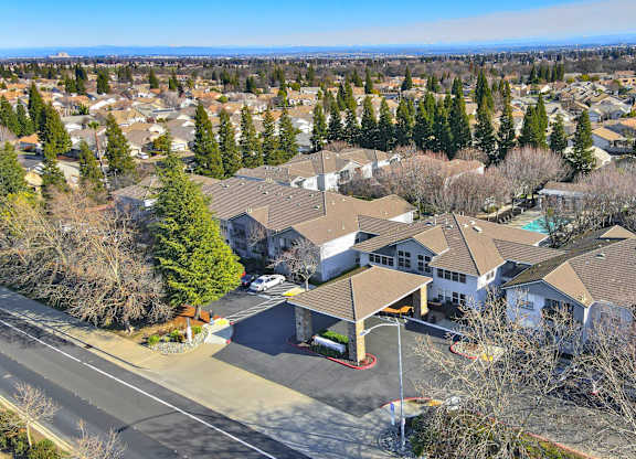 A large white building with a brown roof is surrounded by a lot of trees.