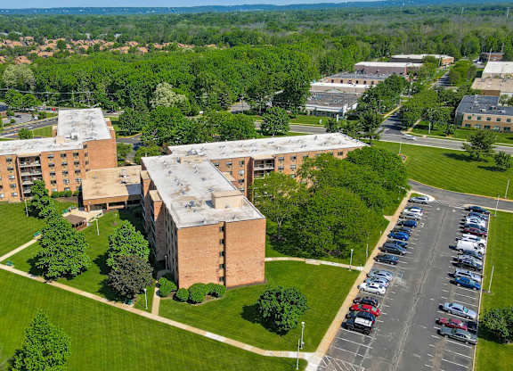 A parking lot is in front of a building with a green lawn in between at Menlo Manor Apartments, New Jersey, 08820