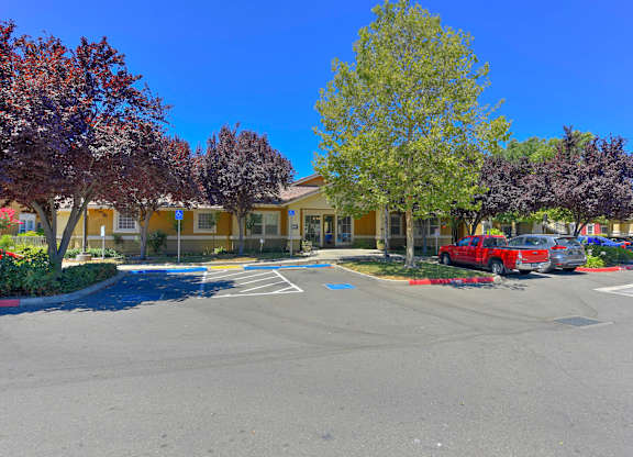A parking lot with a building and trees in the background at Hurley Creek Apartment Homes, Sacramento