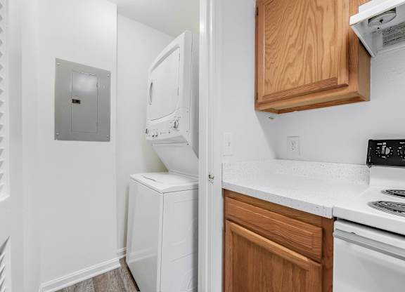 A white stackable washer and dryer sits in area next to a kitchen with wooden cabinets at Acclaim at Sterling, in Sterling, VA
