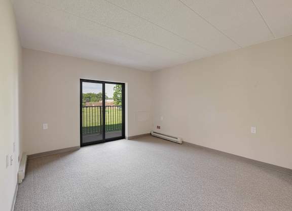 A room with a carpeted floor, a window with a view of a fence, and a door leading outside at Menlo Manor Apartments, New Jersey