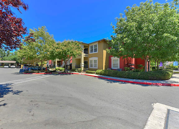 A parking lot with a yellow building in the background at Hurley Creek Apartment Homes, Sacramento, CA, 95834
