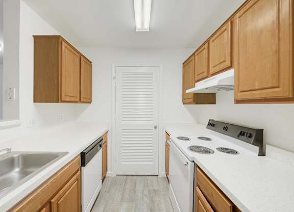 Galley kitchen with wood cabinets and white appliances at Acclaim at Ashburn Apartments, Ashburn, Virginia
