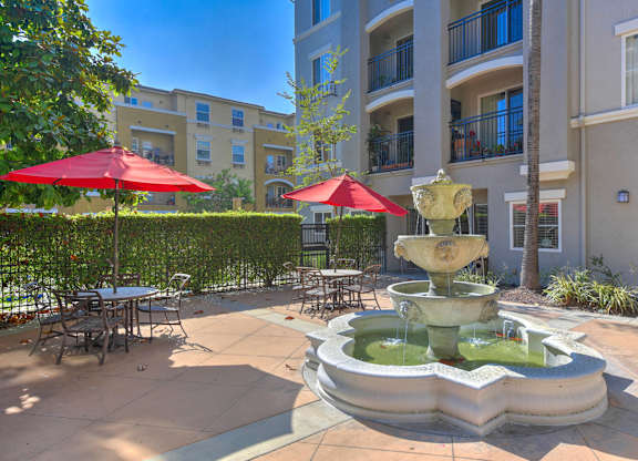 A fountain in the middle of a courtyard with tables and chairs around it.