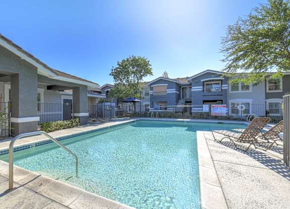 A swimming pool surrounded by chairs and apartment buildings.