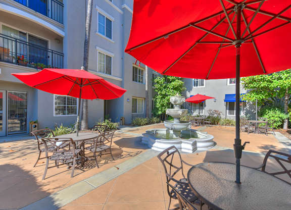 A red umbrella is in the foreground of a patio with chairs and a table.