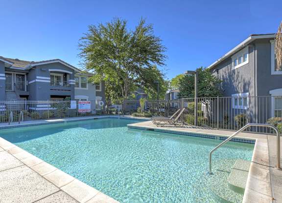 A swimming pool surrounded by a metal fence and a building in the background.