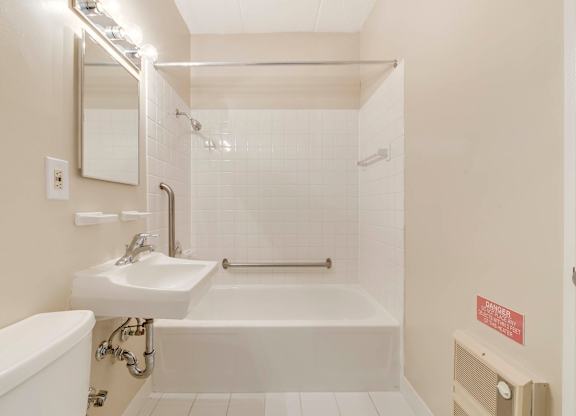 A white bathroom with a tub, sink, and mirror at Menlo Manor Apartments, Edison, New Jersey