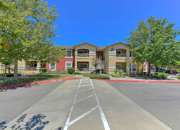 A parking lot in front of a building with a clear blue sky at Hurley Creek Apartment Homes, Sacramento