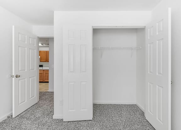 A white door is open to a room with a grey carpet and a large closet with white double doors at Acclaim at Sterling, Sterling, VA