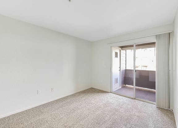 A room with a carpeted floor and a sliding glass door leading to a balcony.