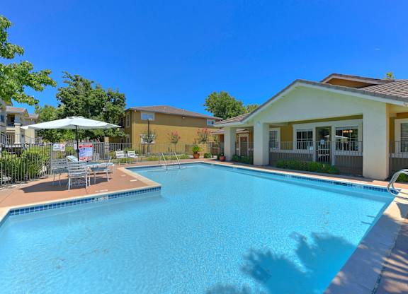 A swimming pool in front of a building with a sun umbrella at Hurley Creek Apartment Homes, Sacramento, CA, 95834