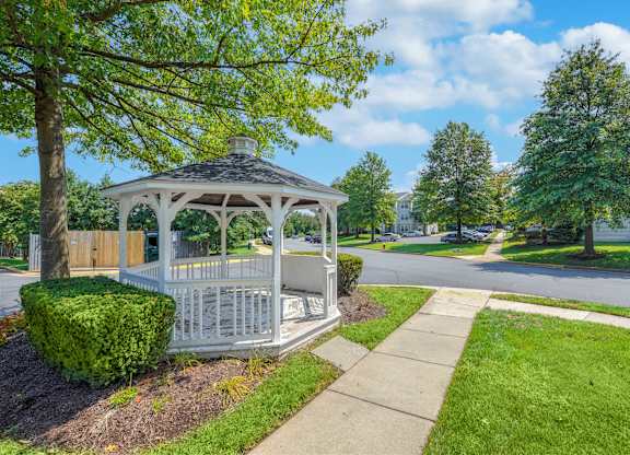 A white gazebo with a black roof is surrounded by greenery and a sidewalk at Acclaim at Sterling in Sterling, Virginia