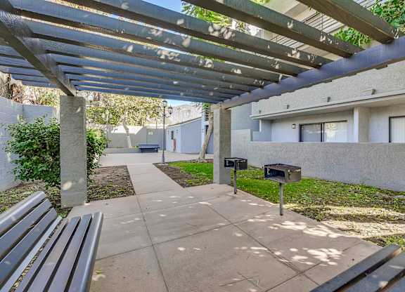 A concrete walkway leads to a mailbox under a metal pergola.