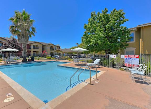 A pool surrounded by chairs and trees with a sign in the background at Hurley Creek Apartment Homes, California, 95834