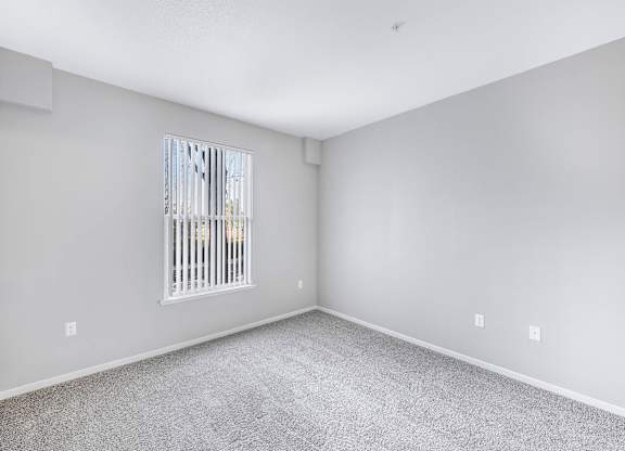 A room with a carpeted floor and a window with bars on it.