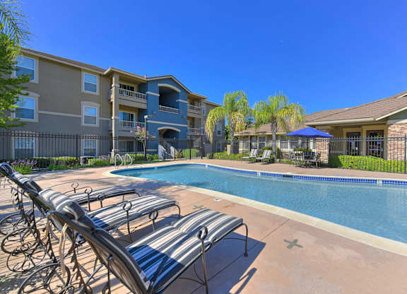 A pool surrounded by sun loungers and apartment buildings.