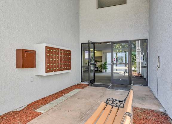 A white wall with a mailbox and a bench in front of it.