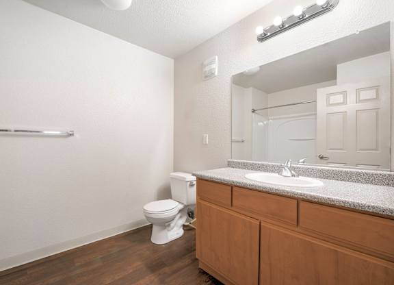 A white toilet sits in a bathroom with a wooden vanity and a mirror at Hurley Creek Apartment Homes, Sacramento, 95834