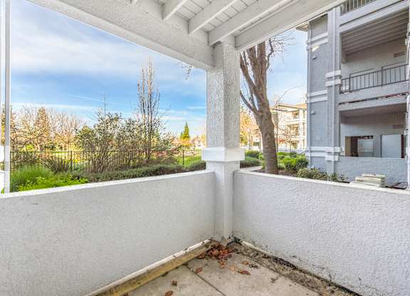 A balcony with white walls and a concrete floor overlooks a residential area.