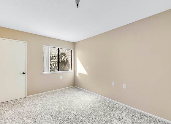 A room with a carpeted floor, a door, and a window with blinds.