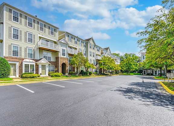 A sunny day at a residential complex with apartment buildings and a parking lot at Acclaim at Sterling, 20164