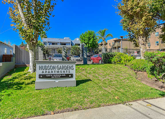A sign for Hudson Gardens Apartments is in the foreground with apartment buildings in the background.