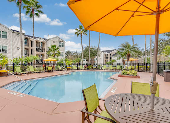 A yellow umbrella is over a table in a pool area.