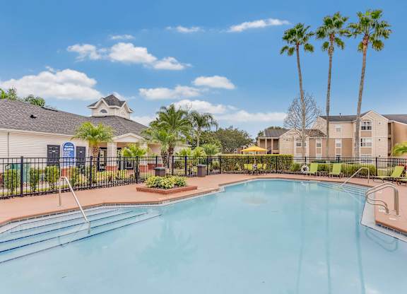 A swimming pool surrounded by palm trees and apartment buildings.