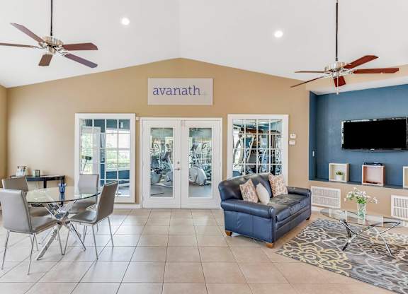 A living room with a glass table and chairs, a blue couch, and a flat screen TV mounted on the wall.