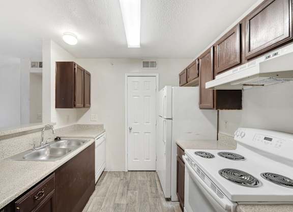 A kitchen with white appliances and brown cabinets. at Cooper's Crossing, Irving, TX