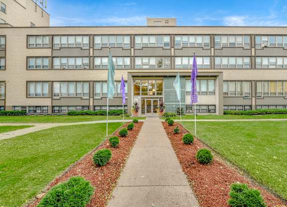A building with a walkway in front of it and flags on either side. at Academy at Drexel Apartments, Illinois, 60637