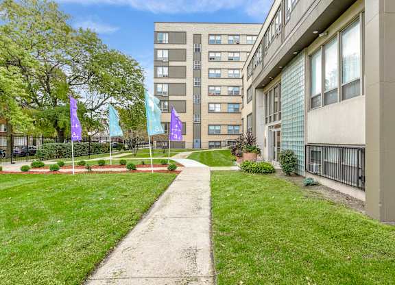 A concrete walkway leads through a grassy area to a building. at Academy at Drexel Apartments, Illinois, 60637