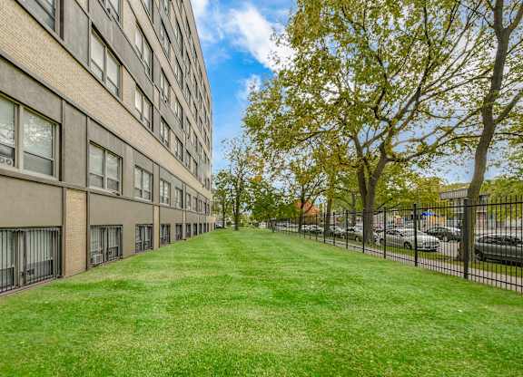 A long grassy area in front of a building with a tree on the right. at Academy at Drexel Apartments, Chicago, IL