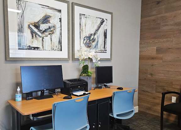 A room with a desk, chairs and two pictures on the wall.
