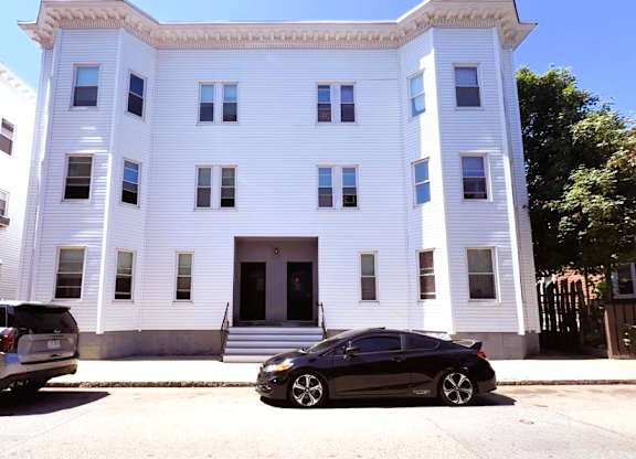 A black car is parked in front of a white building.