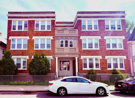 A white car is parked in front of a red brick building.