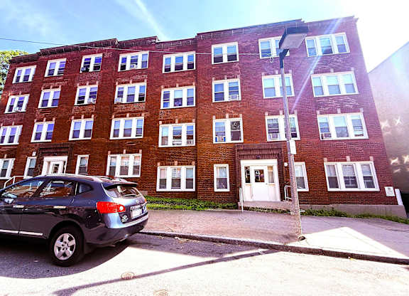 A blue car is parked in front of a red brick building.