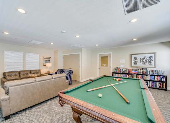 A pool table in a room with a couch and a bookshelf.