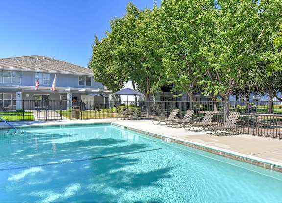 A swimming pool in front of a building with trees and chairs around it.