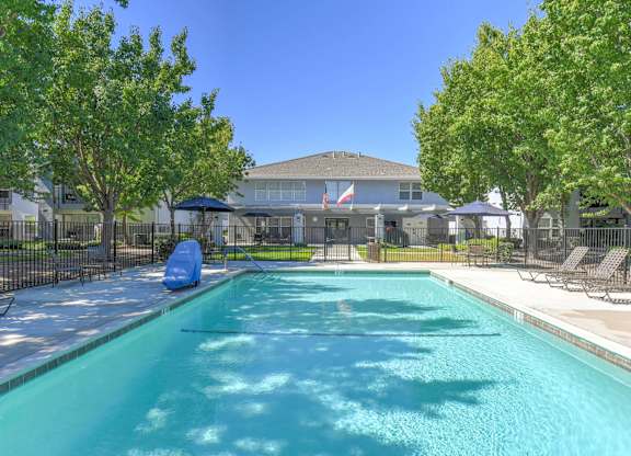 A swimming pool in a residential area with trees and houses in the background.