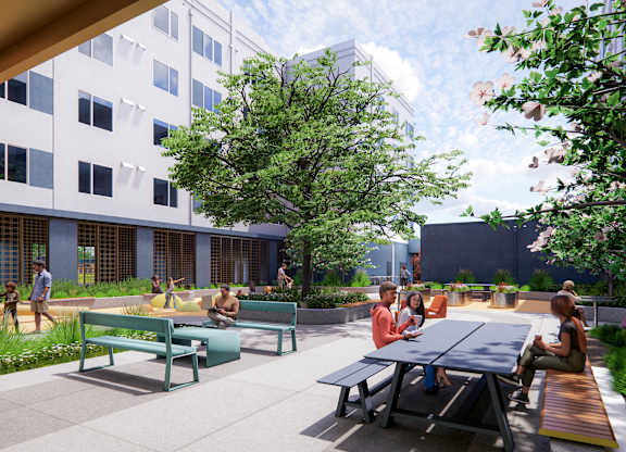 A group of people are sitting and standing around a table in a courtyard at Rivo Apartments, Sacramento