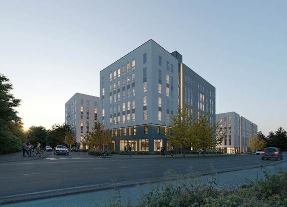A modern building with a glass facade is surrounded by trees and a street with cars and bicycles.