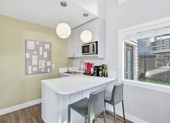 A kitchen with a white counter and grey chairs.