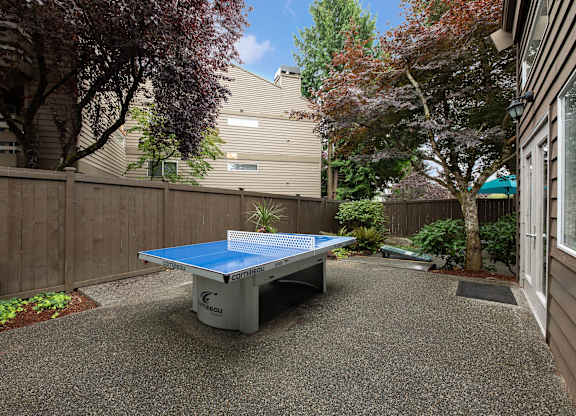 A blue table tennis table is in the middle of a gravel area.