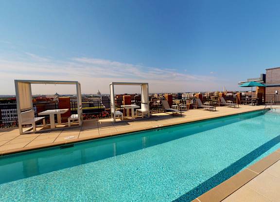 A large outdoor swimming pool with sun loungers and a building in the background.
